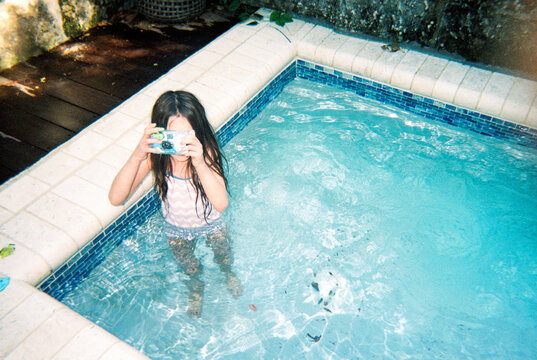 Child in swimming pool takes photo with disposable film camera