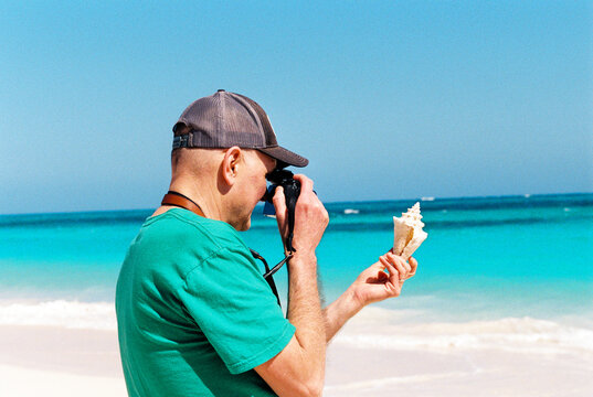 Man on vacation photographs a shell he found on a tropical beach