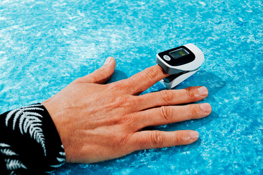 the index finger of a man holds a fingertip pulse oximeter