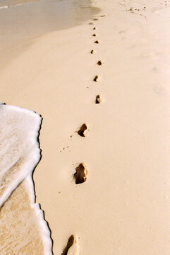 Footprints in the sand on a tropical beach with wave coming in