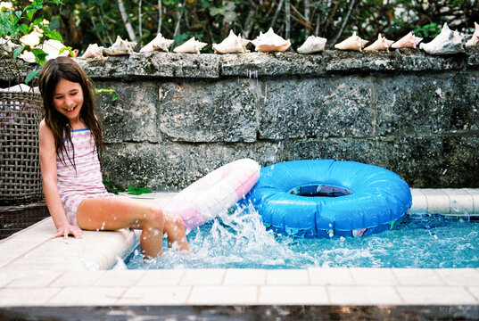 Girl smiles while splashing in a swimming pool with her feet