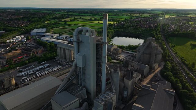 Aerial view of Rugby Cement Plant featuring tall chimneys, industrial silos, and surrounding green fields during golden hour in Rugby, England, United Kingdom.