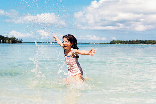 Happy girl on vacation splashes in the water on a beach in Bahamas