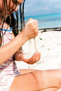 Child playing on beach pours sand between her fingers