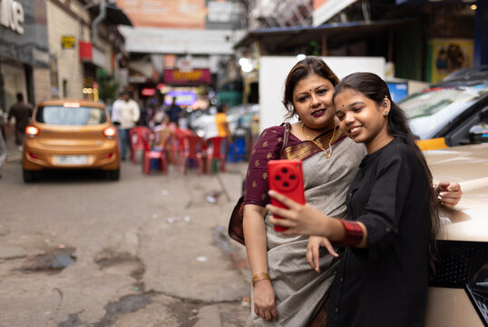 Indian mother and daughter taking selfie standing in a busy road