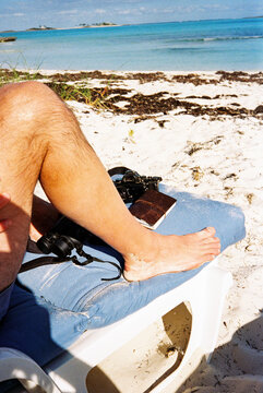 Detail of man's legs on beach chair with vacation objects