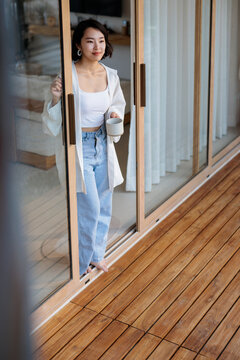 Woman with coffee looks out from glass doors.