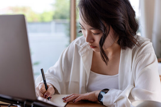 Woman working at desk with laptop and notebook.