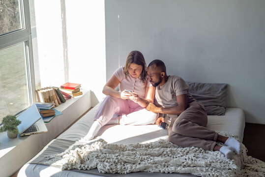 Interracial couple relaxing at home on a bed with phones