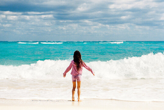 Girl on Bahamas beach holds her arms open to incoming waves