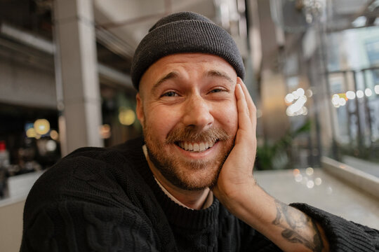 Beaming young man smiling with beard, beanie, and tattoo