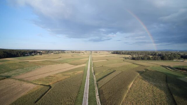 Drone shot of train track in Slovenia countryside with farming fields and rainbow.