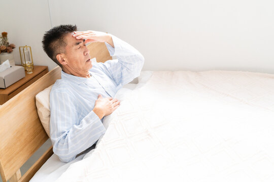 ベッドの上で頭を押さえる男性
