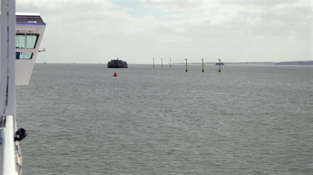 Ferry POV across The Solent toward Spitbank Fort with buoys, cargo ship and cloudy horizon