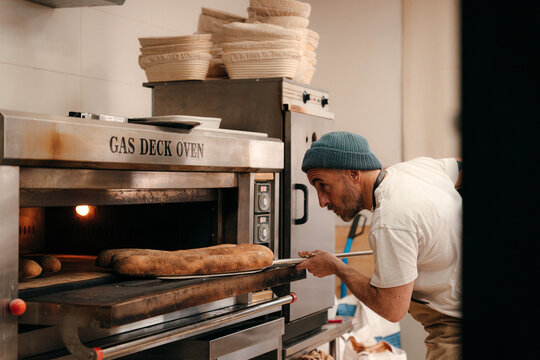 Baker Checks Bread in Gas Deck Oven in Bakery Kitchen