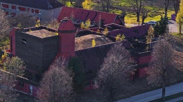 Decaying, desolate structure with damaged roofs and invading nature on golden hour in aerial view
