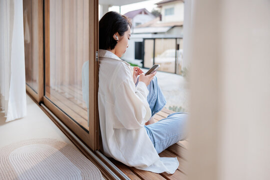 Woman with phone sits by window, modern home.