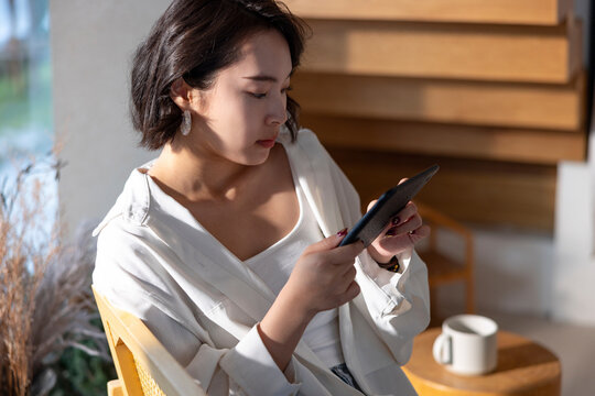 Woman in white shirt using tablet in bright room.