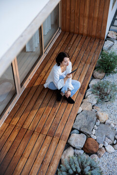 Woman on deck with phone, rocks, and plants.