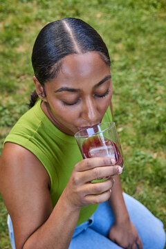 Young woman sipping a cocktail sitting on the grass outside