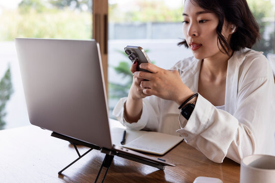 Woman using phone while working on laptop at desk.