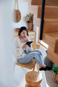 Woman reading e-reader and drinking coffee in bright room.