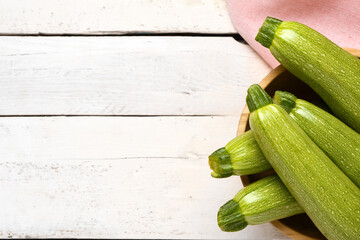 Bowl with many fresh green zucchini on white wooden background