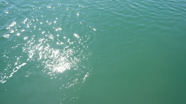 Silent turquoise sea surface changing with whirlpool and sparkling sunlight from cruise ship
