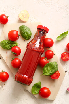 Board with glass bottle of ketchup and tomatoes on white background
