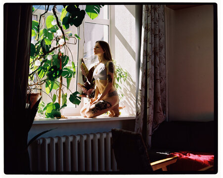Woman sitting by window with plants during daytime