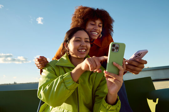 Women using smartphone together on rooftop smiling and sharing