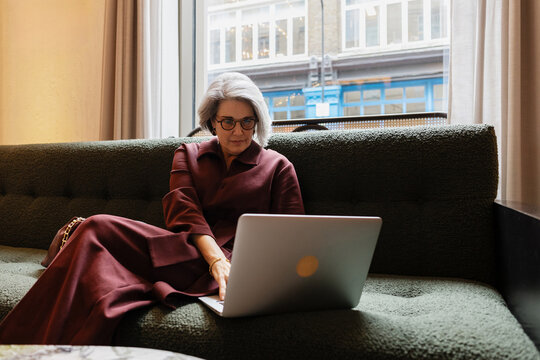 Senior woman working on laptop comfortably on sofa