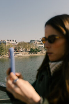 Blurred close-up of a woman using her smartphone over the Seine River
