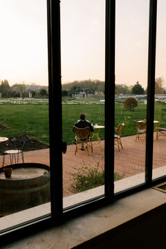 Man drinks and reads outside a hotel, seen through a large window