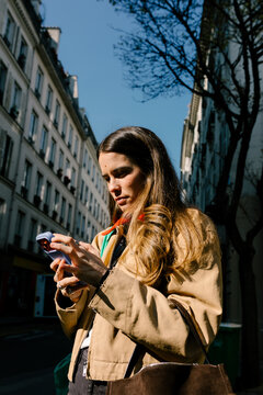 Woman standing on a sunny street in Paris while using her smartphone