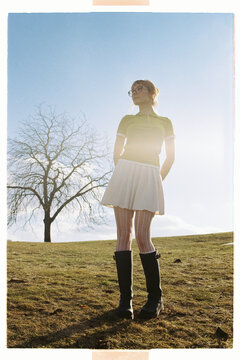 Young girl stands on grassy field under bright sky near bare tree