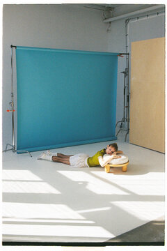A girl lies on a simple stool in a studio with a blue backdrop
