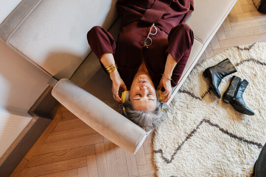 Content senior woman relaxing on sofa enjoying music headphones