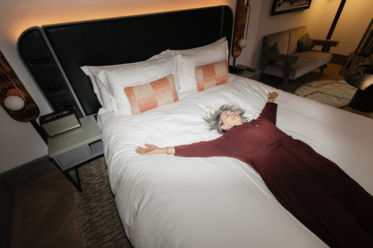 Senior woman relaxing horizontally on bed with arms spread