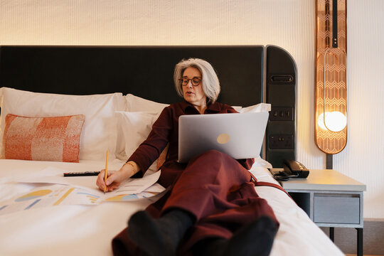 Professional using laptop and analyzing documents in hotel bed