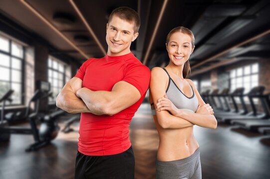 Fitness couple standing back to back with arms crossed in a modern gym interior
