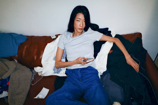 Person relaxing on sofa with clothes using smartphone
