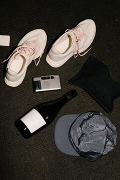 Sneakers, film camera and wine bottle on dark carpeted floor