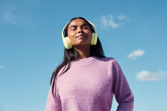 Woman listening to music with headphones outdoors under blue sky