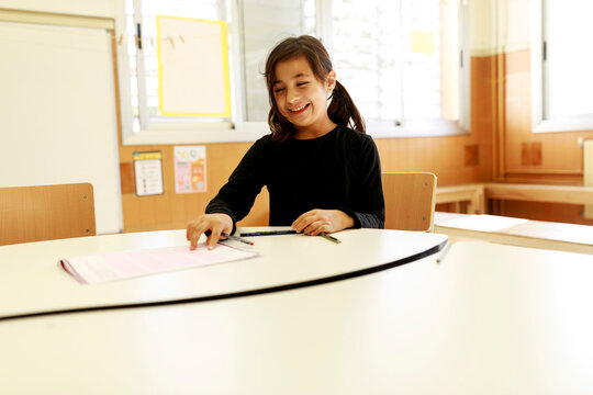 Girl Sits at Table Marking Paper in Bright Classroom During Day