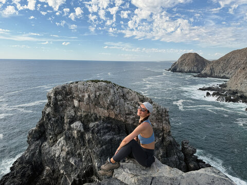 female sitting on cliff by the ocean