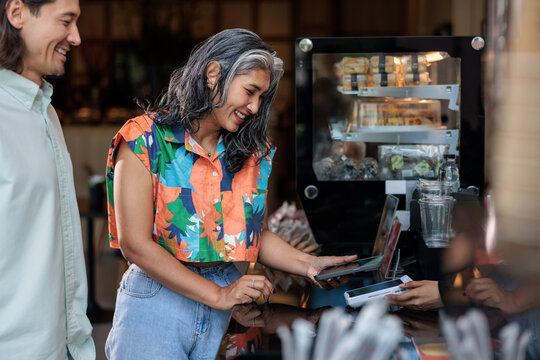 Woman pays with phone at cafe counter, man smiles.