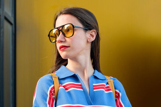 Woman in sunglasses against bold yellow wall