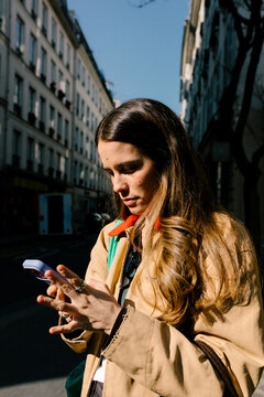 Woman standing on a sunlit Paris street, focused on her smartphone
