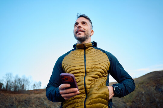 Casual man stands outdoors, holding his phone